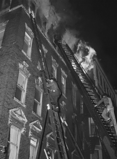 A 1970s fire scene: All in a day's work. The jake on the right will move the 2 1/2" line through the window dressed as you see him here - no fire coat, boots or gloves, just his helmet and a Dungaree jacket. Bill Noonan photo/FireFotos.com